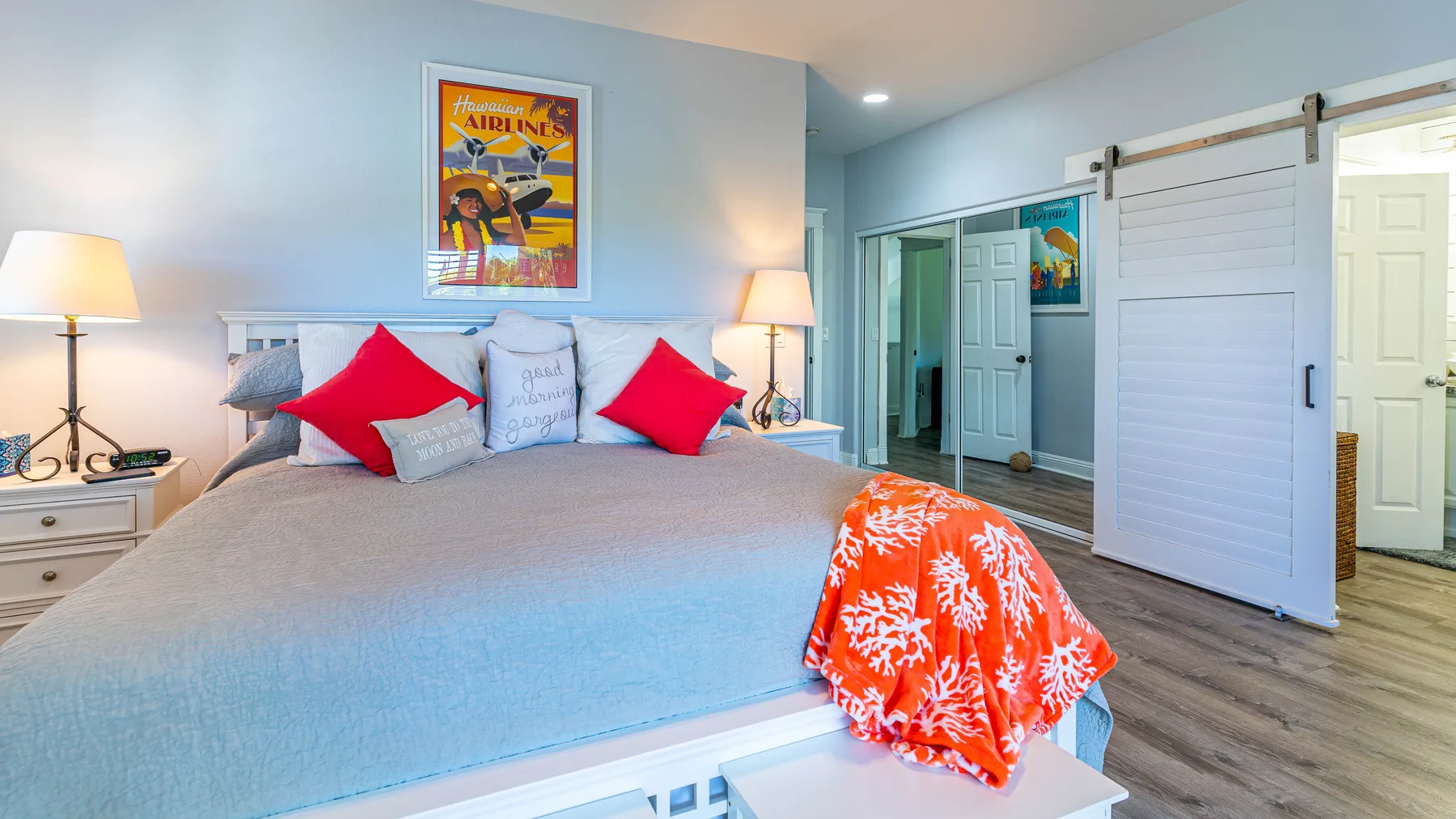 Un dormitorio con una cama vestida con ropa de cama clara y cojines rojos.