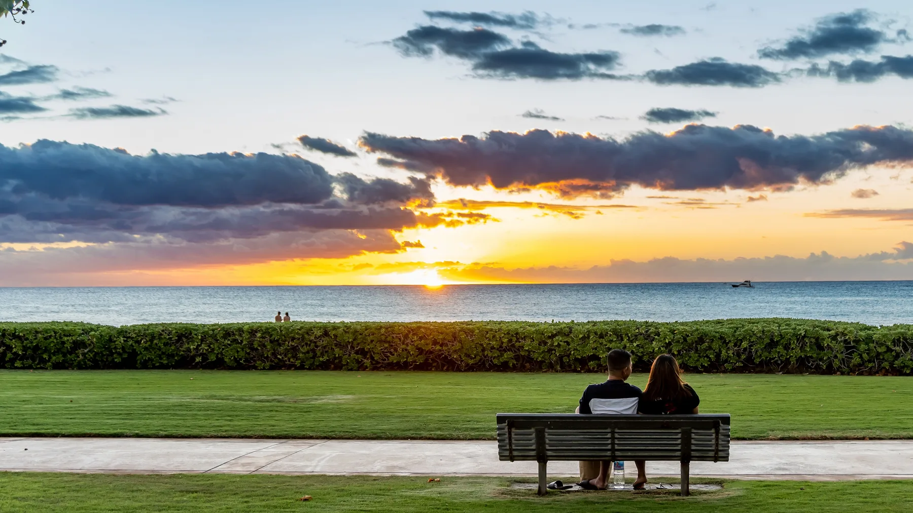Una pareja se sienta en un banco frente al mar al atardecer.