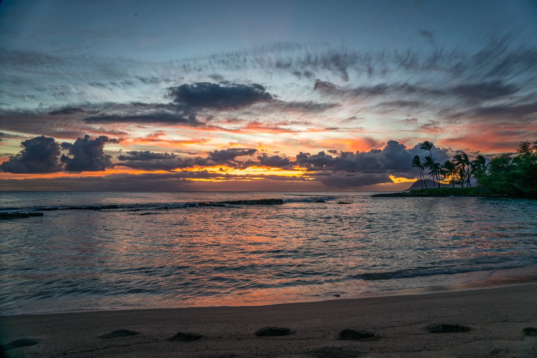 Una playa tropical al atardecer, con palmeras junto a la orilla.