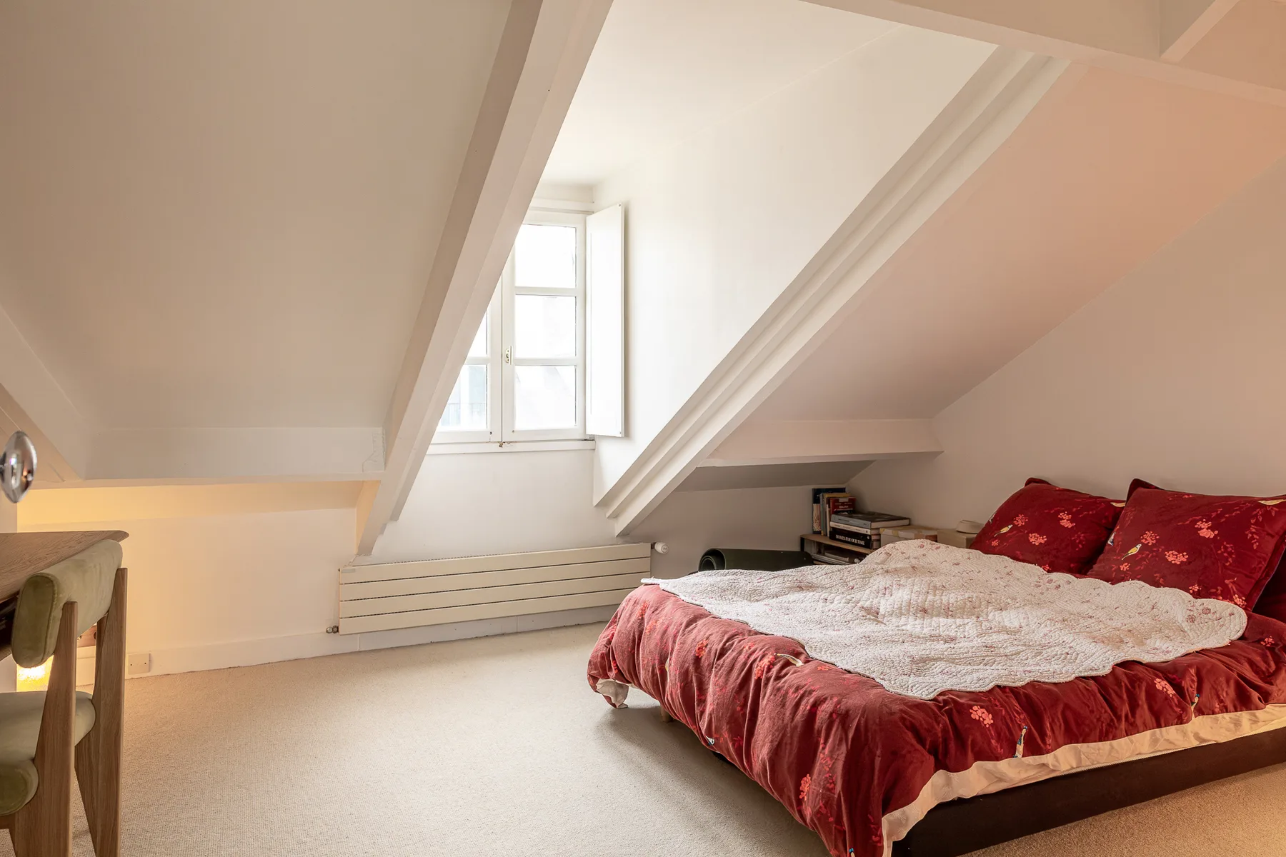 Dormitorio con una cama bajo techos inclinados y una ventana.