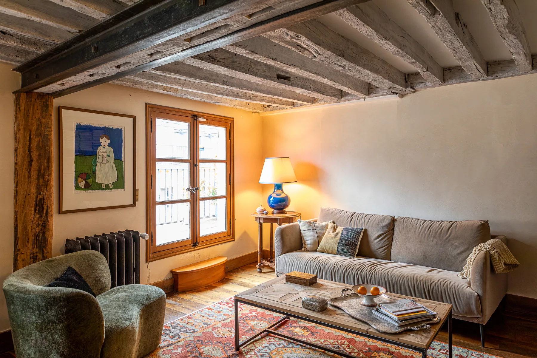 Una sala de estar con asientos, una mesa de centro y una ventana bajo vigas expuestas.
