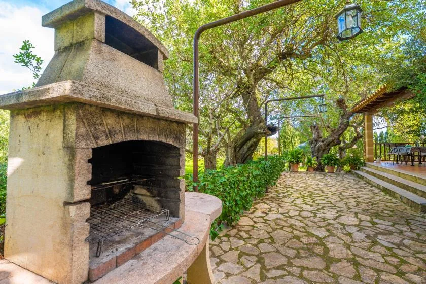 Un patio de jardín empedrado con una chimenea exterior bajo árboles frondosos.