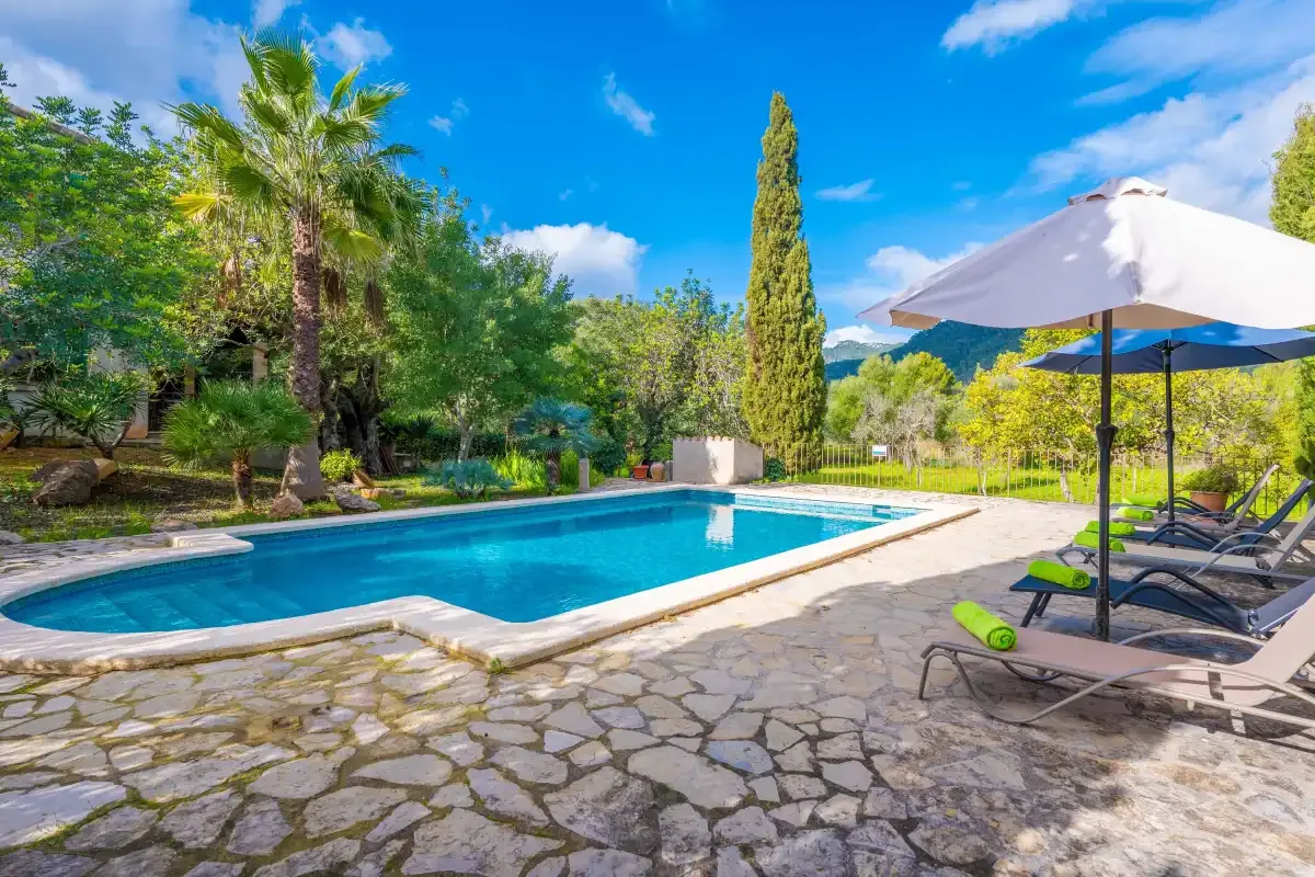 Una piscina junto a un patio de piedra con tumbonas y sombrillas.
