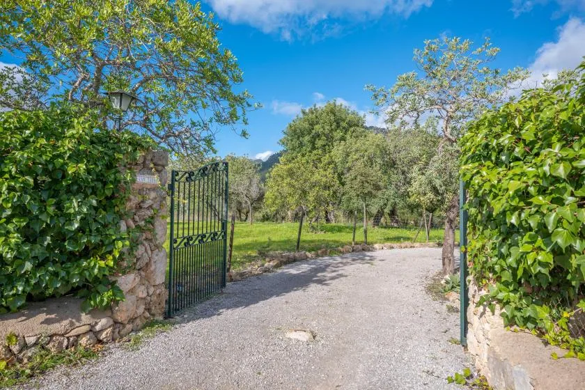 Una entrada abierta al jardín da a un camino de grava entre árboles y vegetación.