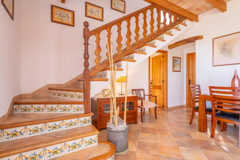 Una escalera con azulejos sube junto a una mesa de comedor de madera en un interior luminoso.