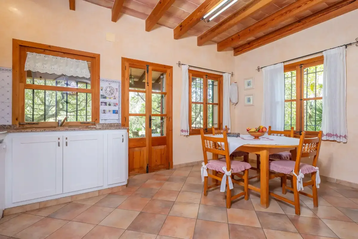 Un comedor con una mesa de madera y sillas está junto a ventanas luminosas.