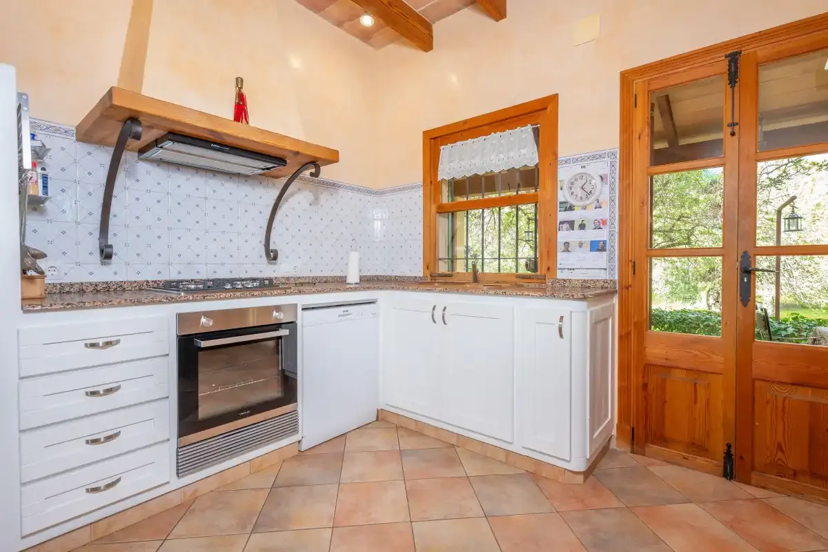 Una cocina luminosa con armarios blancos, horno integrado y ventanas con marcos de madera.