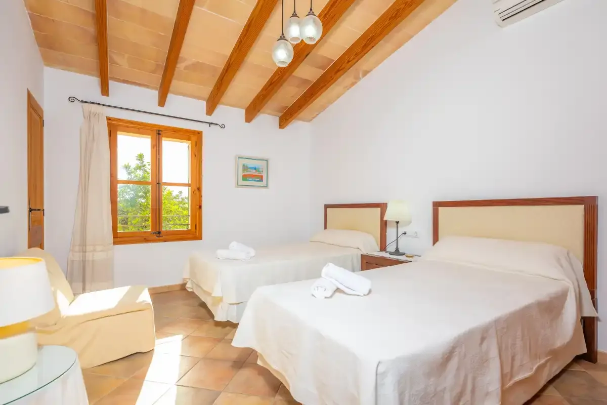 Un dormitorio luminoso con dos camas, vigas de madera vistas y una ventana.