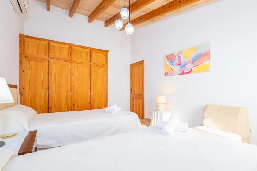Un dormitorio luminoso con ropa de cama blanca, armarios de madera y vigas expuestas.