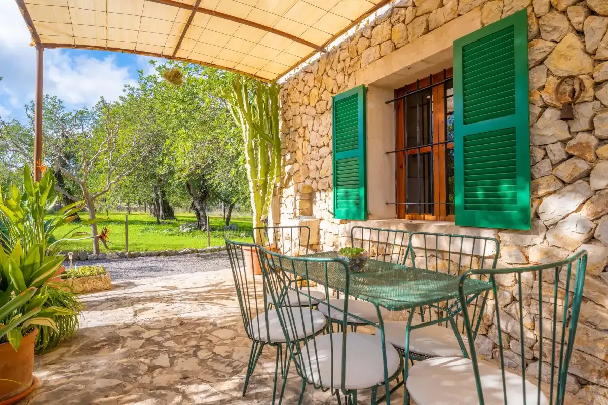 Una zona de comedor al aire libre junto a un muro de piedra, con contraventanas verdes y vistas al jardín.