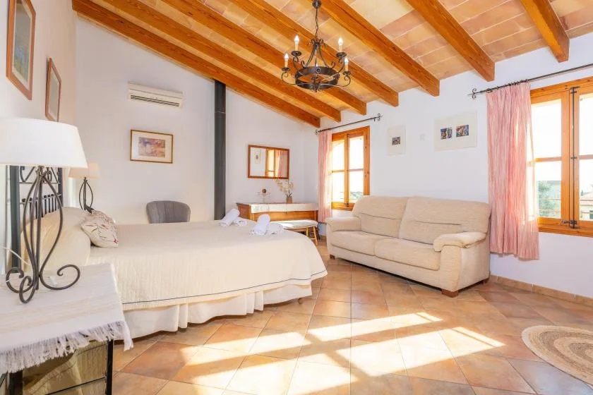 Un dormitorio luminoso con una cama, asientos y ventanas soleadas.