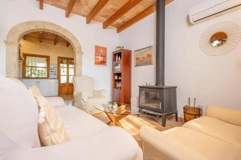 Una sala de estar luminosa con una estufa de leña y asientos bajo vigas de madera vistas.