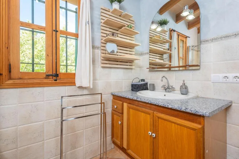 Un mueble de baño con lavabo está bajo un espejo de pared, junto a una ventana.