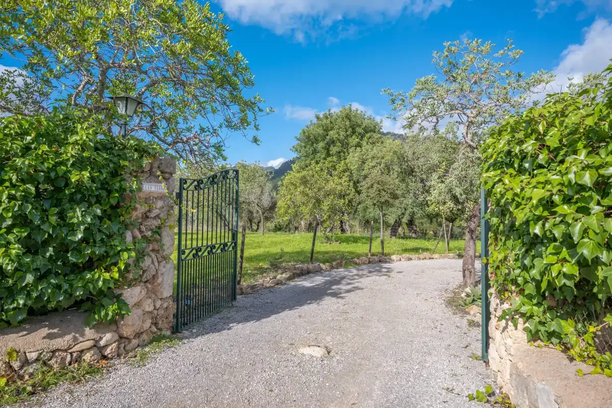 Entrada a un jardín con una puerta metálica abierta y un camino de grava.
