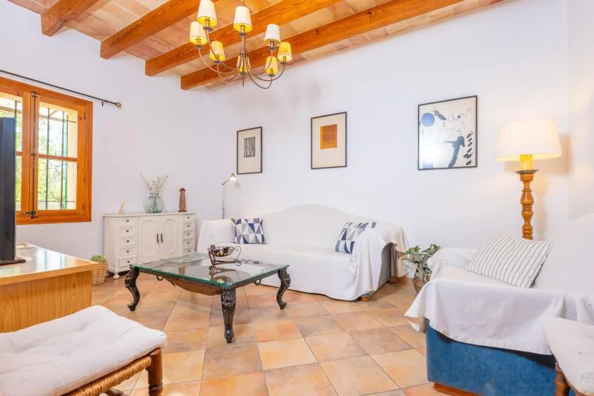 Una sala luminosa con asientos cubiertos, una mesa de centro de vidrio y vigas de madera expuestas.