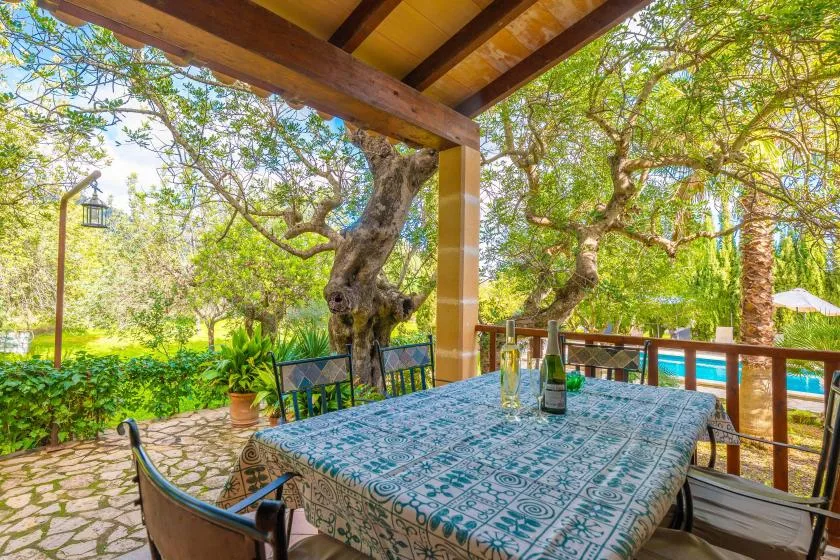 Un comedor exterior cubierto da a un jardín y una piscina.