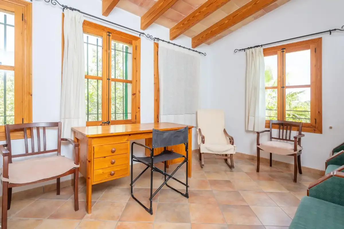 Una habitación luminosa con escritorio de madera, asientos y ventanales.