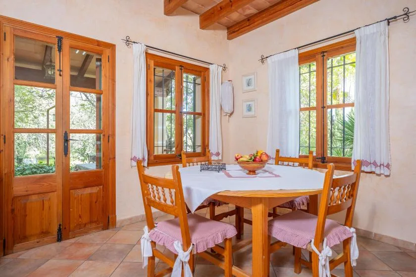 Un comedor con una mesa de madera, sillas y ventanas grandes.