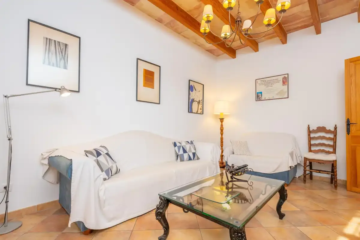 Una sala de estar con asientos cubiertos de blanco, una mesa de centro de vidrio y vigas de madera a la vista.