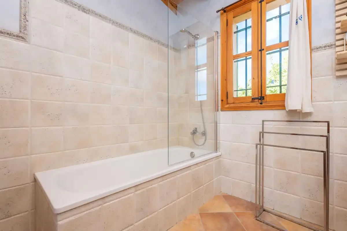 Un baño con bañera, ducha y ventana con marco de madera.