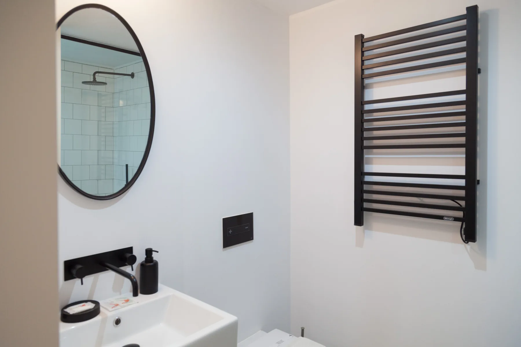 Un baño con lavabo, espejo ovalado y toallero calefactor en la pared.
