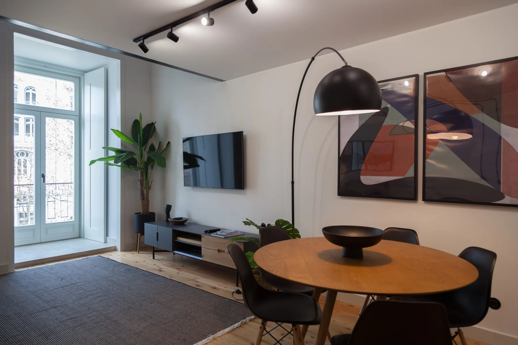 Una sala de estar y comedor modernos con mesa redonda, televisor en la pared y grandes ventanas.