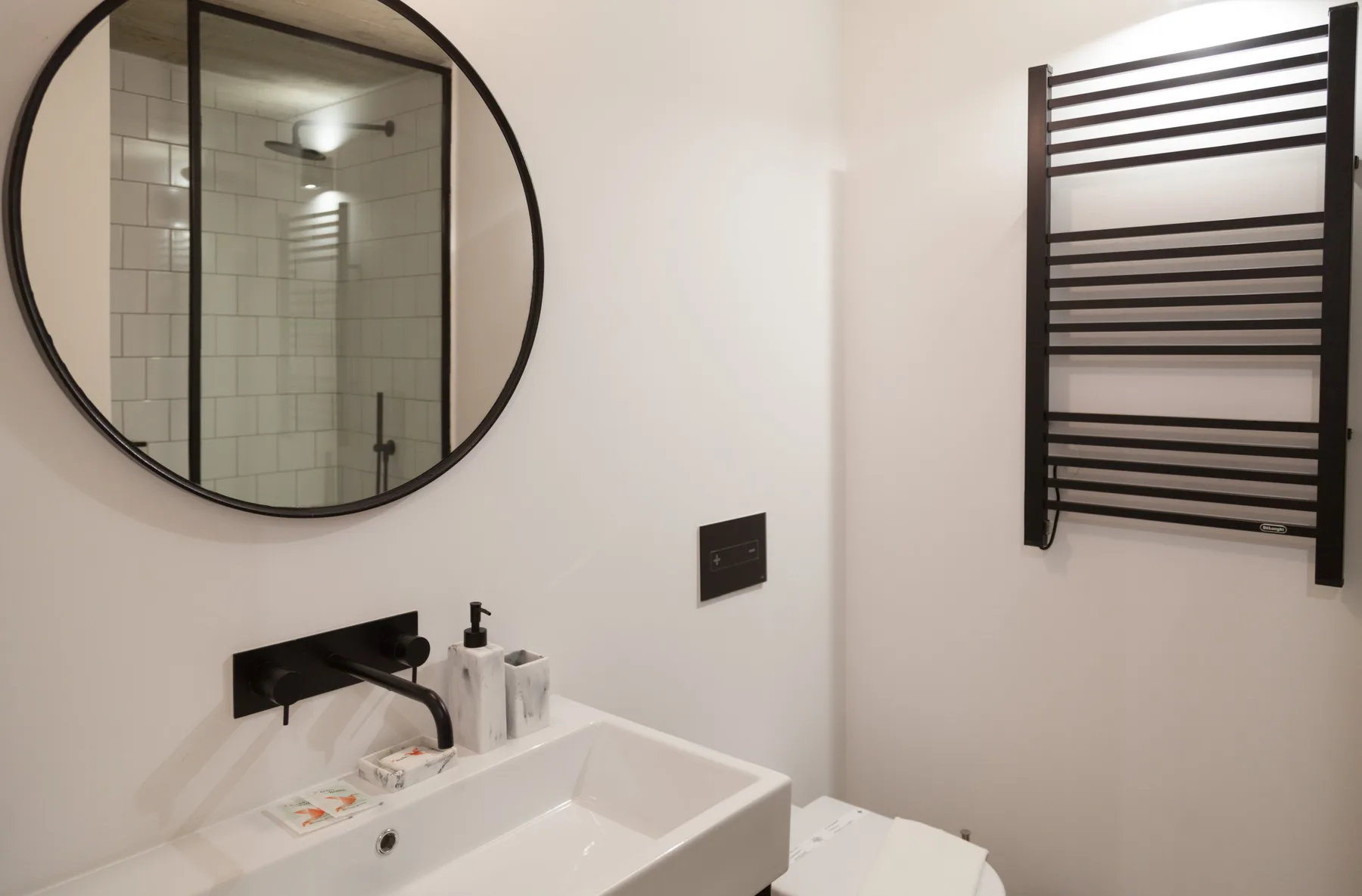 Un baño con lavabo, espejo redondo y toallero montado en la pared.