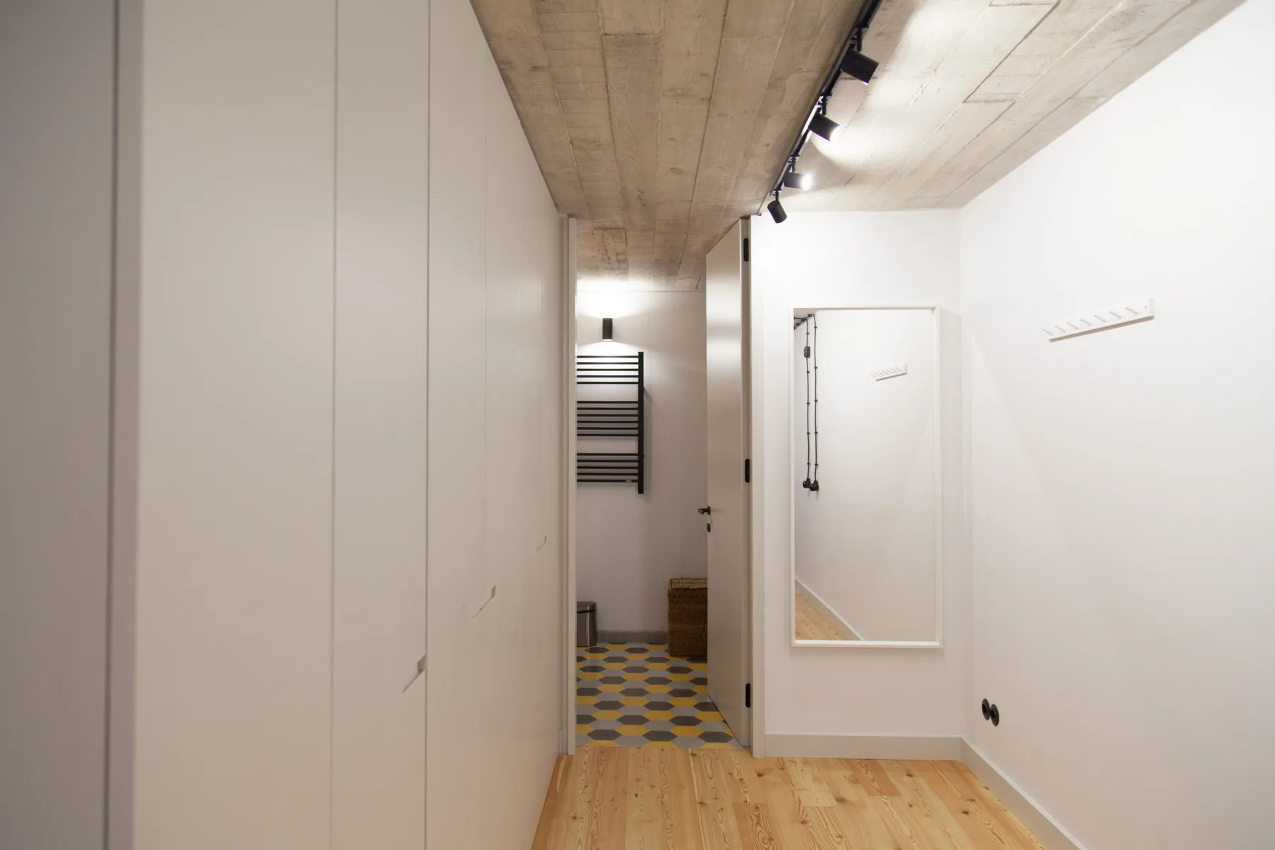Un pasillo interior estrecho con suelo de madera clara y paredes blancas.