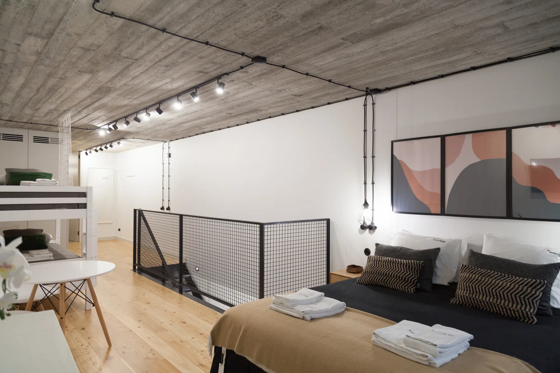 Un dormitorio tipo loft con una cama junto a una barandilla metálica negra y una zona de estar abierta.