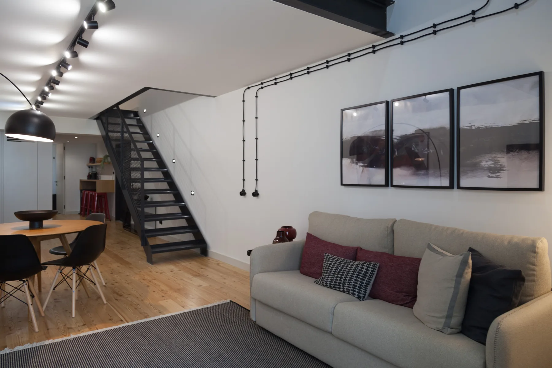 Sala de estar con un sofá, cuadros enmarcados y una escalera junto al comedor.