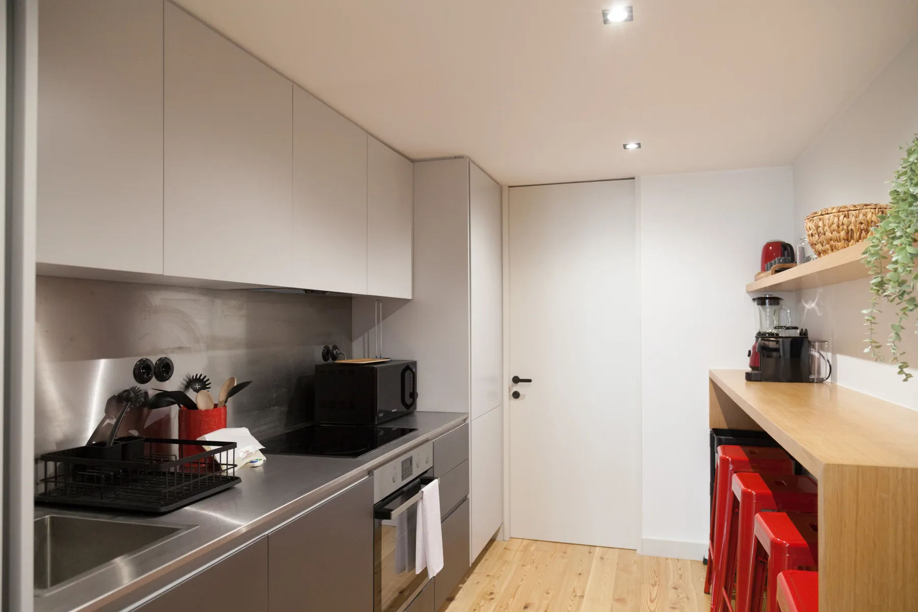 Una cocina moderna y compacta con encimeras de acero inoxidable y suelo de madera clara.