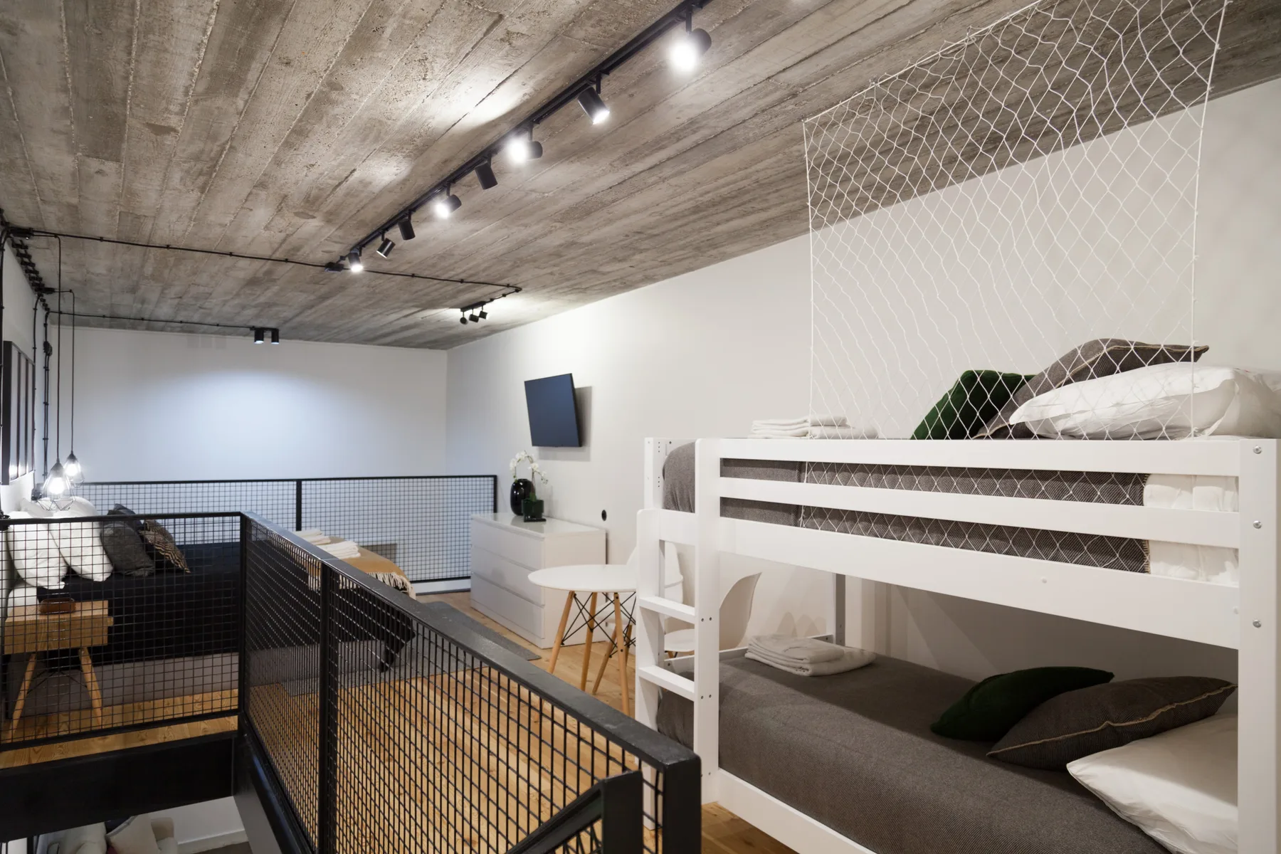 Un dormitorio tipo loft con literas y una barandilla metálica en el nivel superior.