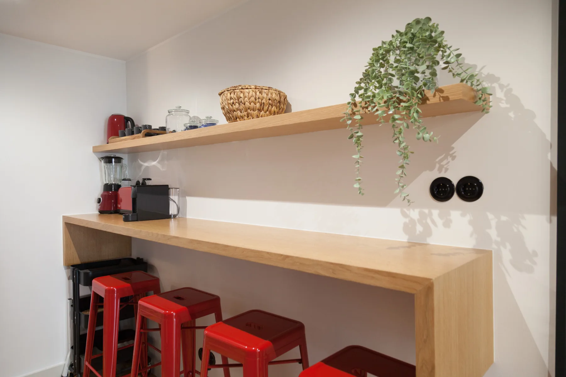 Una cocina compacta con una barra, taburetes rojos, electrodomésticos y plantas en una repisa.