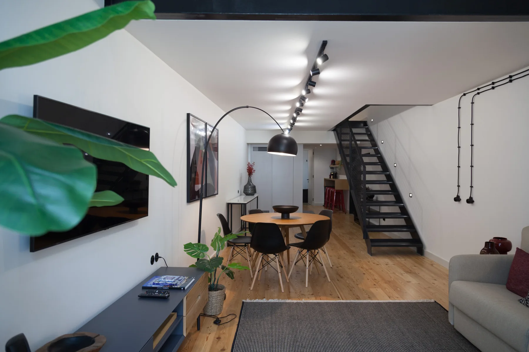 Una sala de estar y comedor modernos con una escalera y un televisor en la pared.