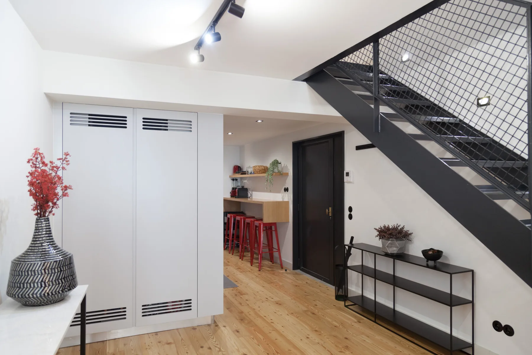Entrada luminosa de un apartamento con una escalera negra y una consola estrecha.
