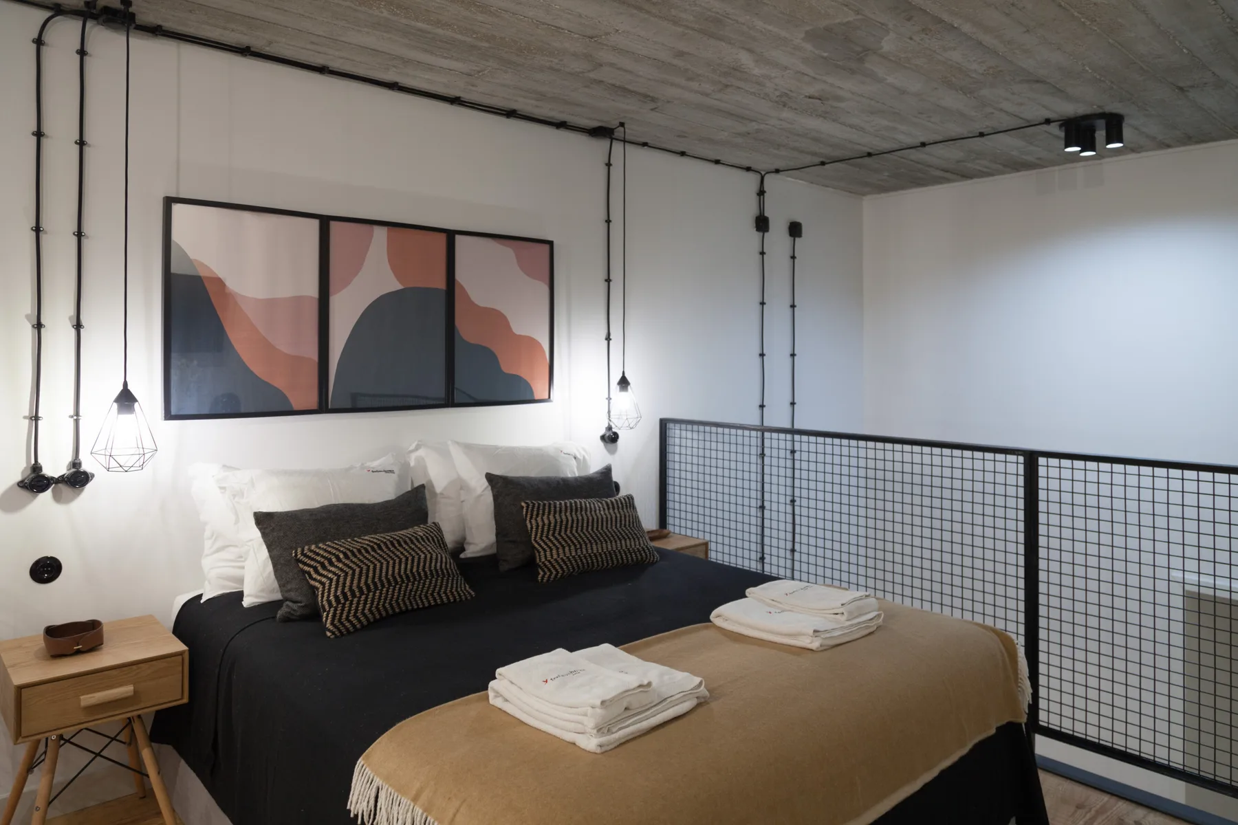 Un dormitorio con una cama bajo una obra abstracta y una barandilla de malla.