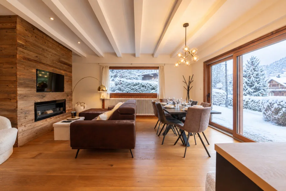 A living and dining room with seating, a table, and large windows overlooking a snowy landscape.