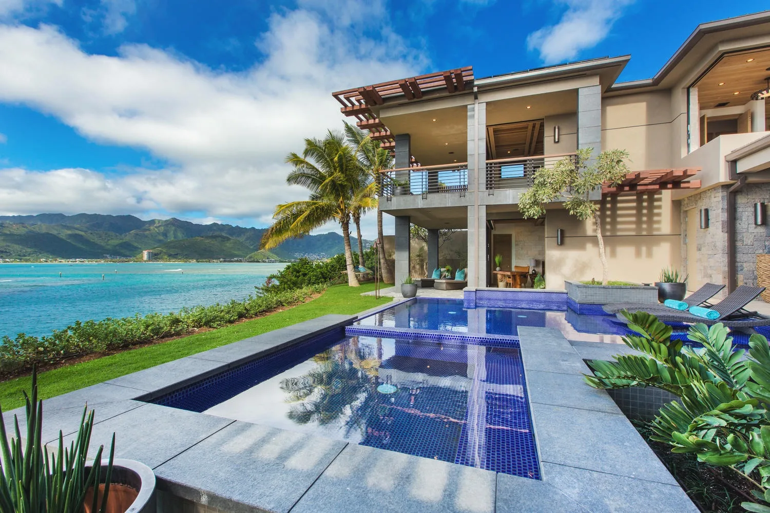 A waterfront villa overlooks a pool, with mountains across the bay.