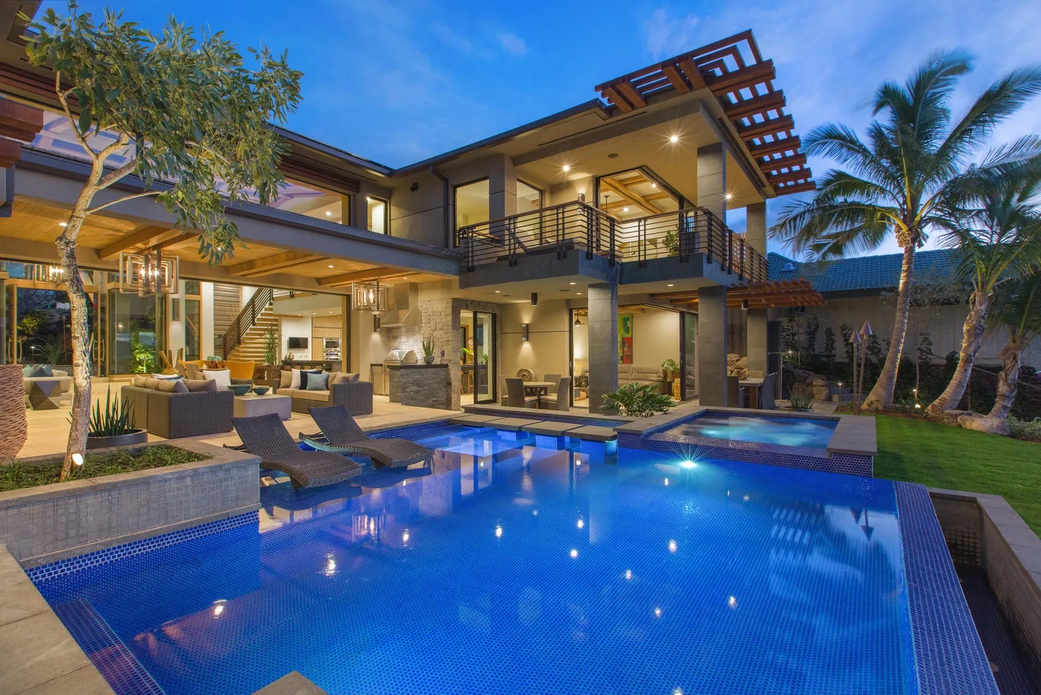 A modern house overlooks a blue swimming pool and landscaped garden.