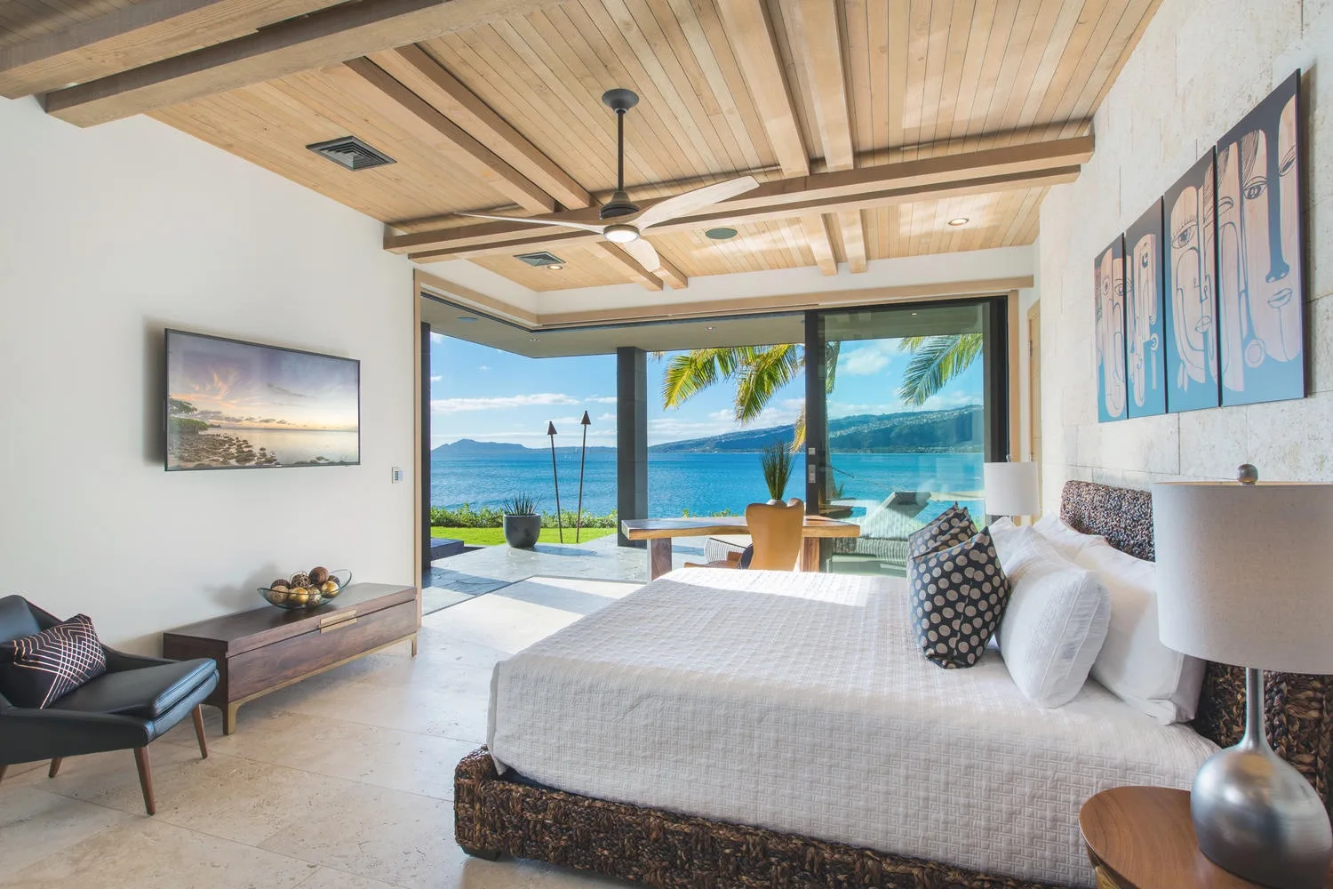 A bedroom with a large bed facing open glass doors and a view of the sea.