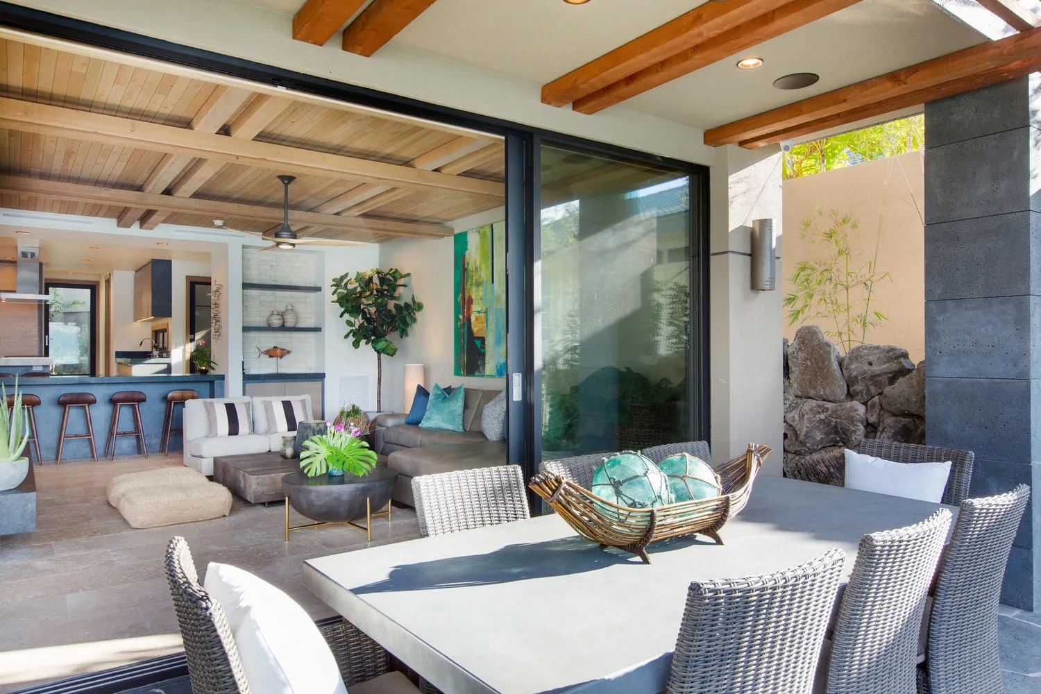 An open-air dining patio with woven seating beside a bright living room.