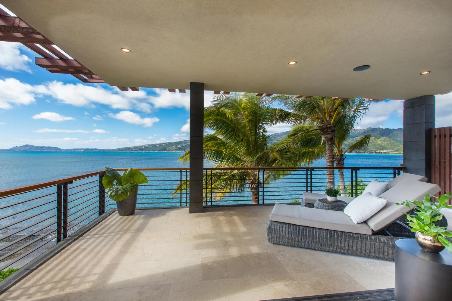 A covered terrace overlooks the water, with outdoor seating and palm trees nearby.
