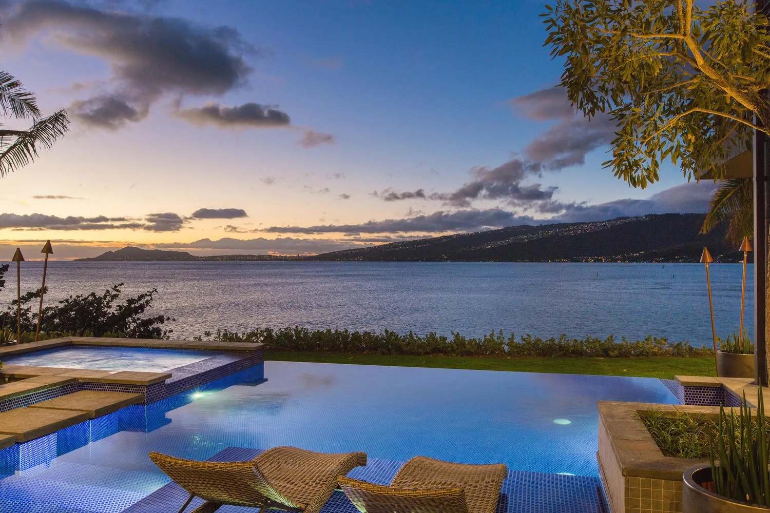 An outdoor swimming pool overlooks a broad body of water at sunset.