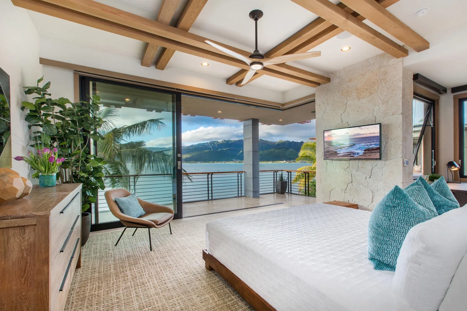 A bedroom opens onto a balcony with views of the water and surrounding hills.