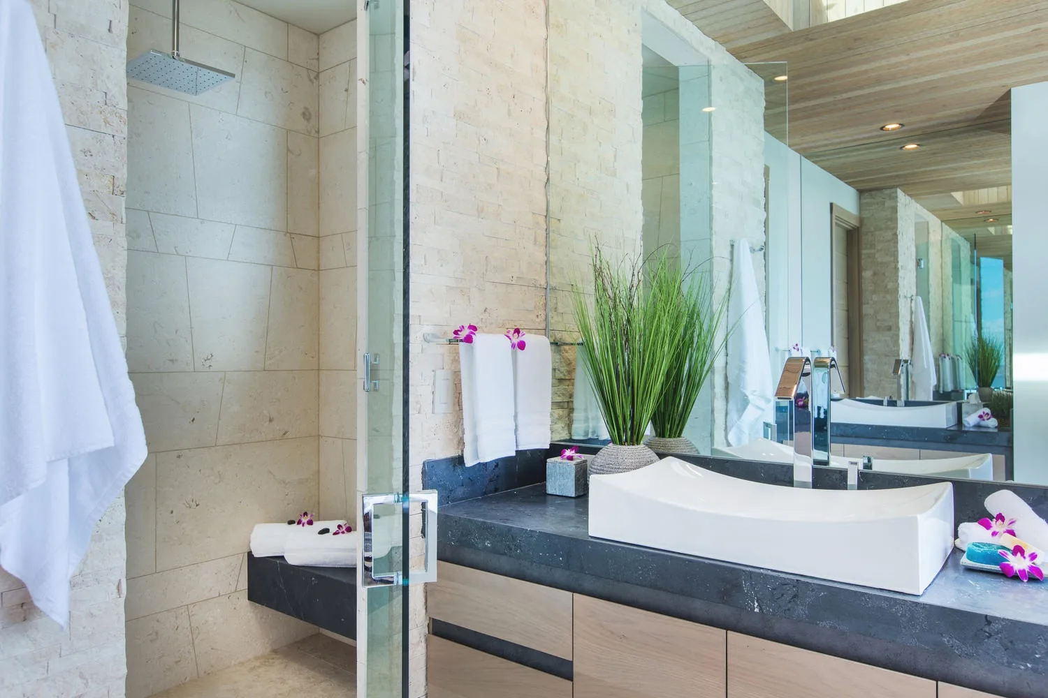 A modern bathroom with a glass shower and a wide vanity topped by a vessel sink.