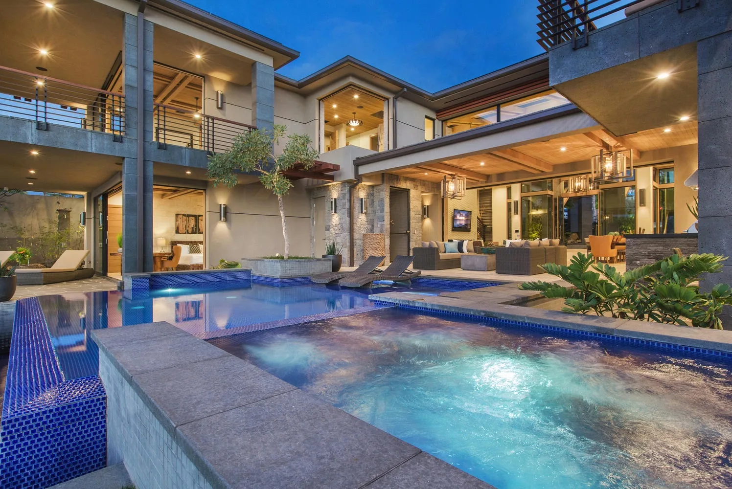 A modern house opens onto a swimming pool and a covered outdoor seating area.