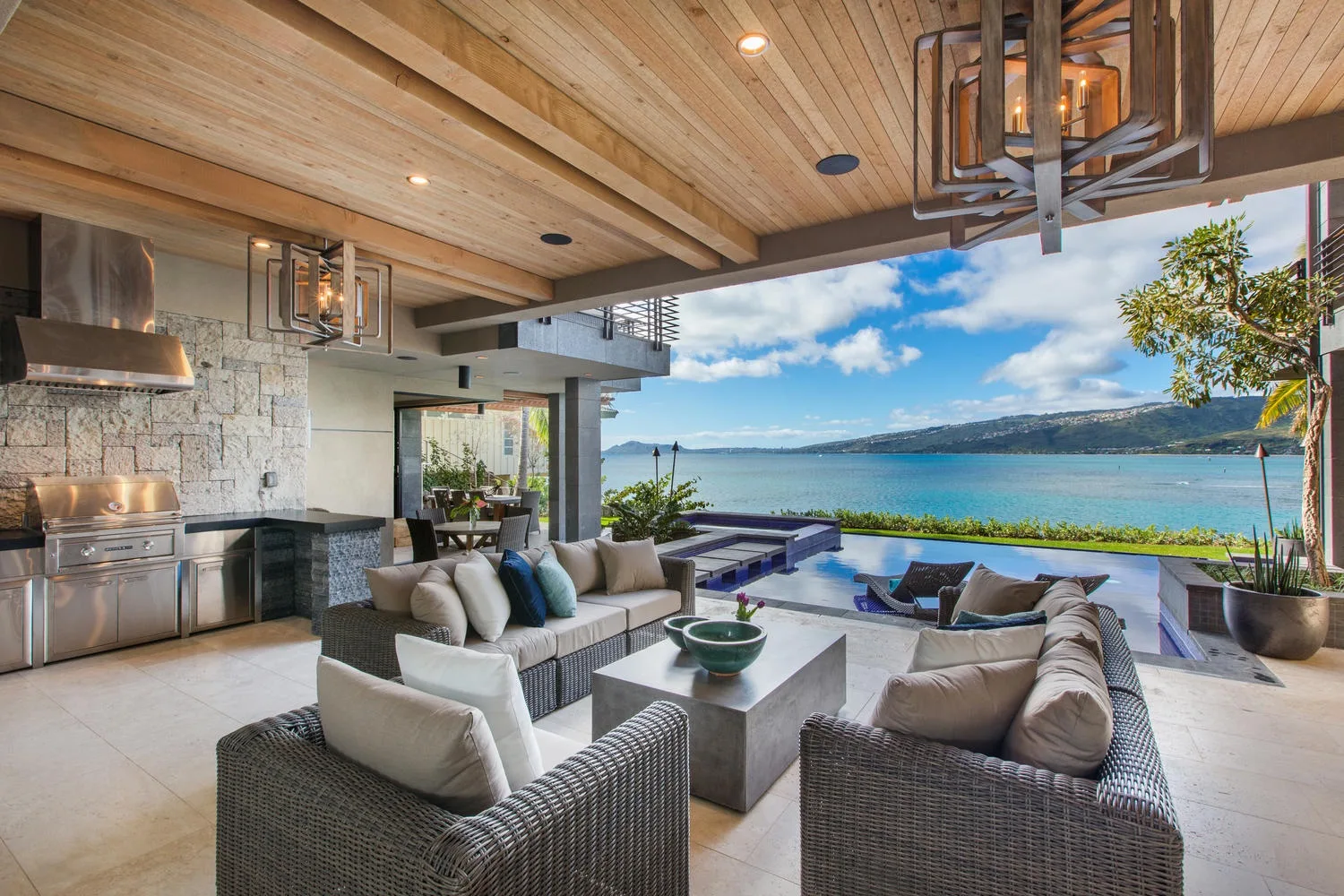An open-plan living area with lounge seating beside a pool and waterfront view.