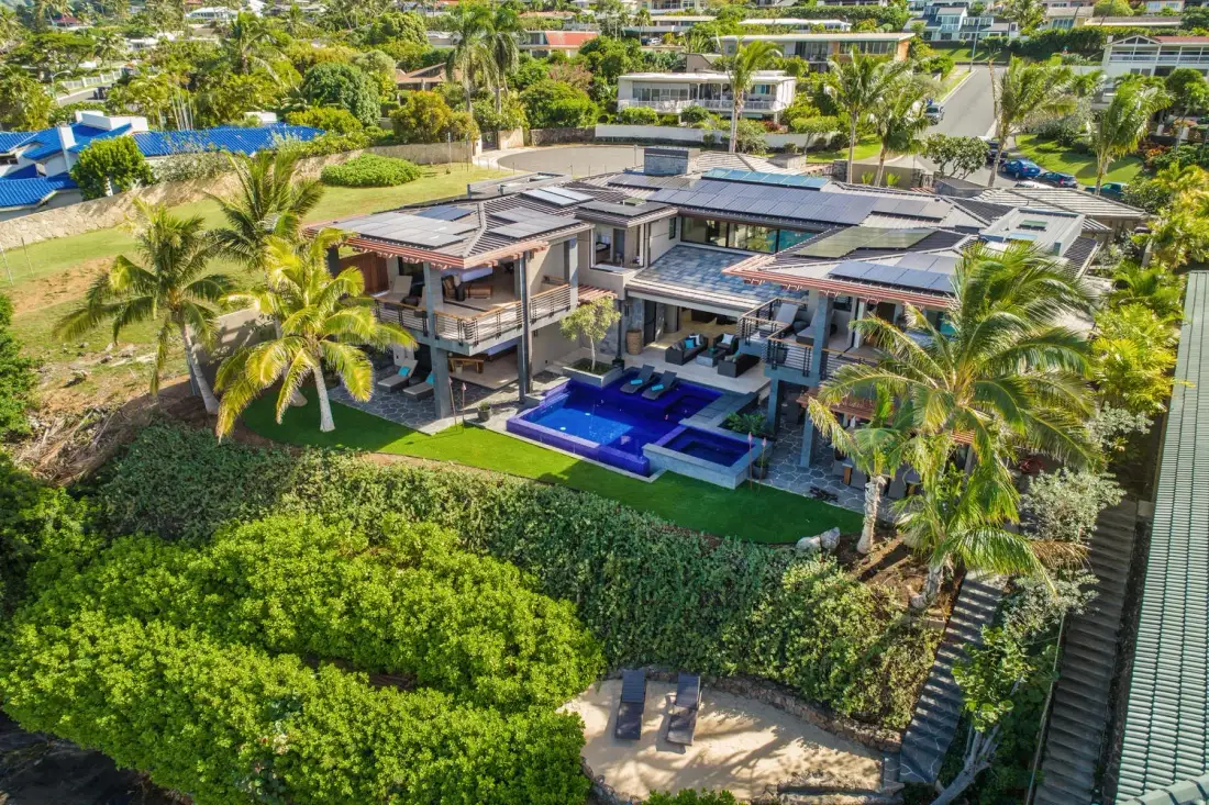 An aerial view of a modern house with a pool surrounded by palms and greenery.