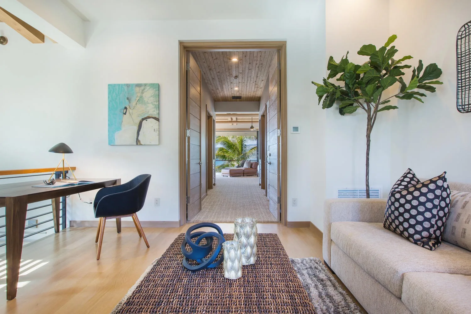 A bright living room with a desk, seating, and a view down the hallway.