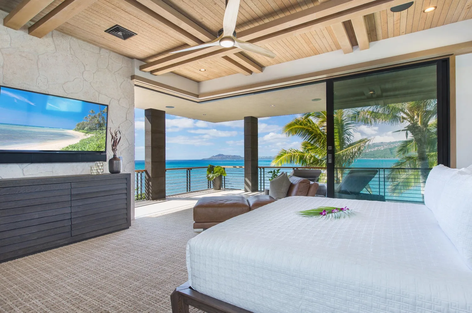 A bedroom opens onto a balcony overlooking the ocean, with a bed and seating area.